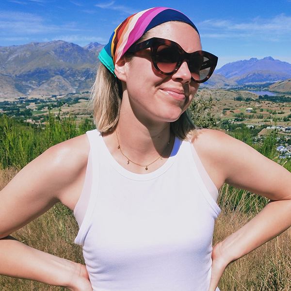 Abby standing in front of a New Zealand mountain background wearing sunglasses and a bandana