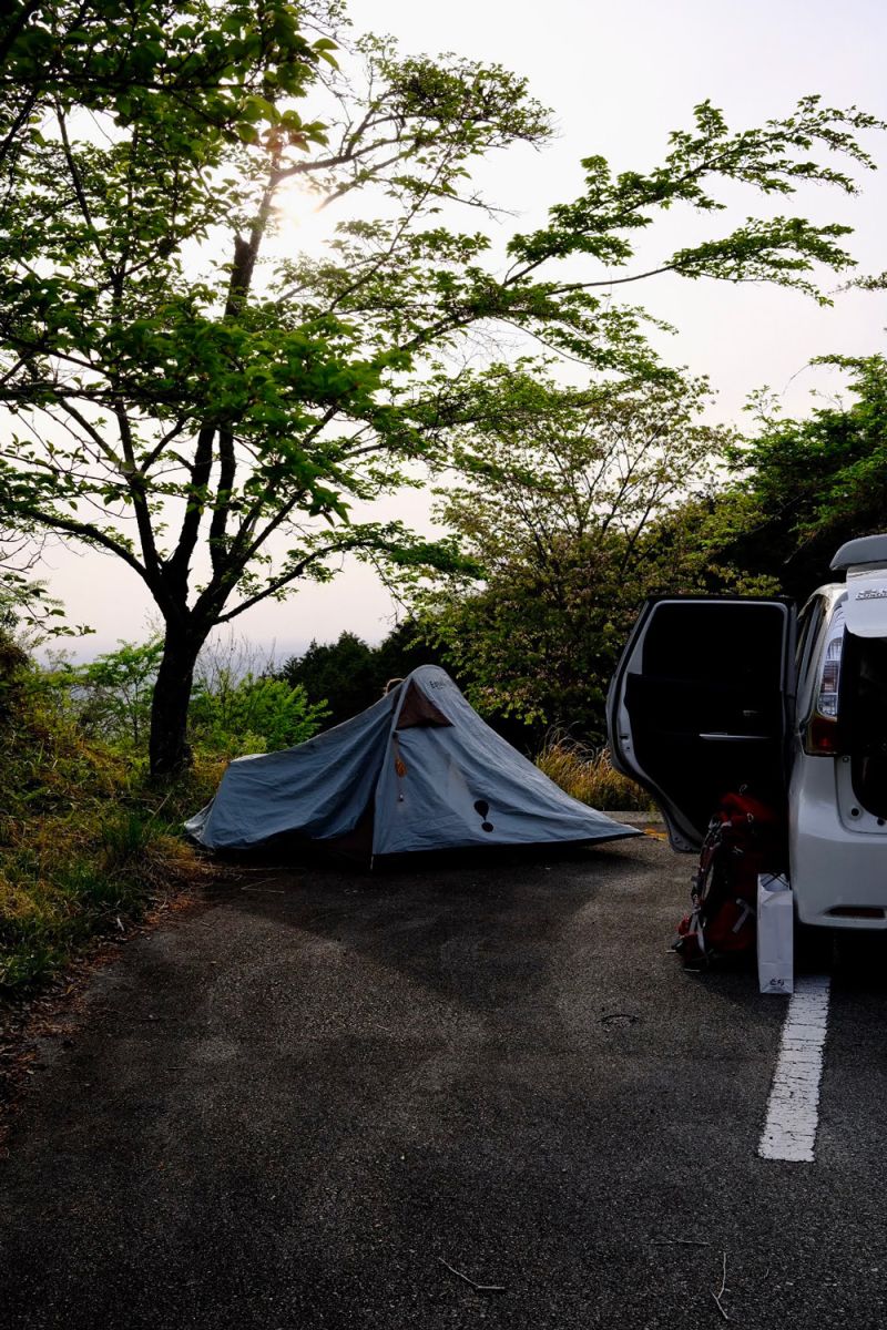 Tent pitched in a car park next to a car next to a tree