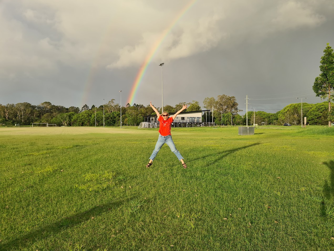 Abby jumping in front of a rainbow on a grass field