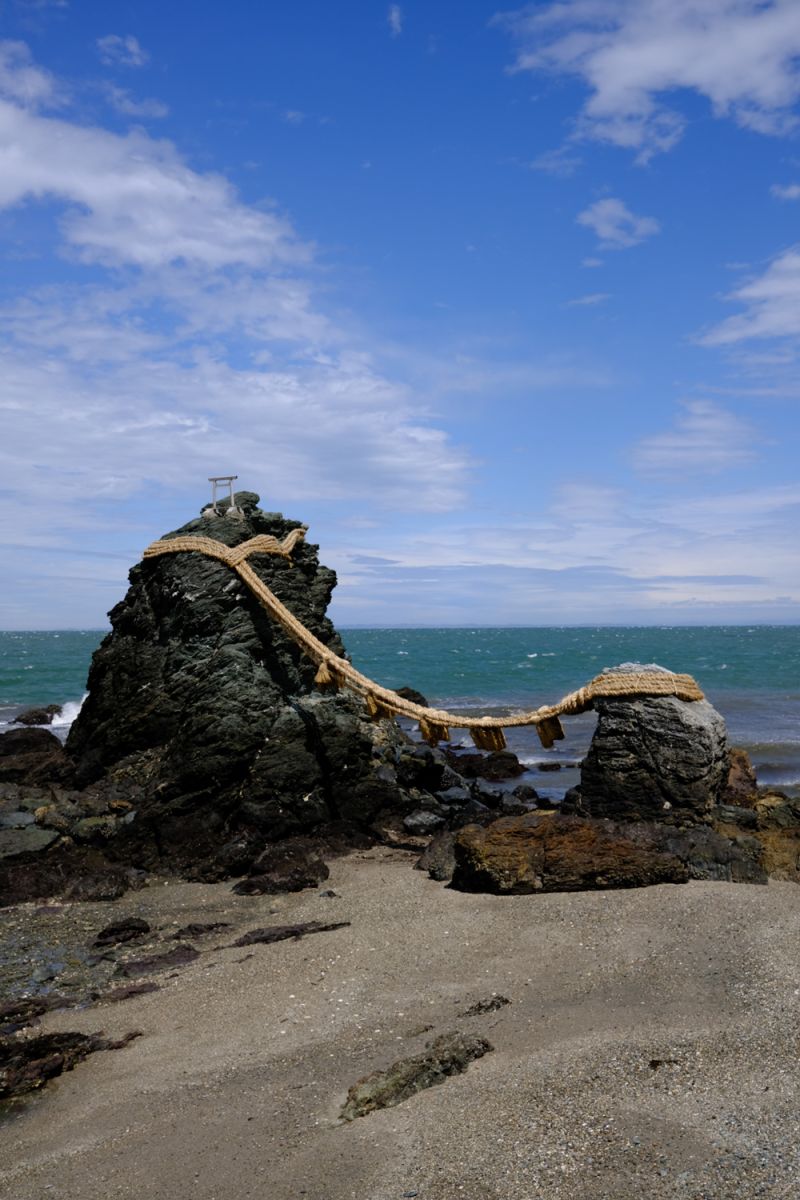 Two rocks on a beach with a traditional Japanese shimenawa straw.