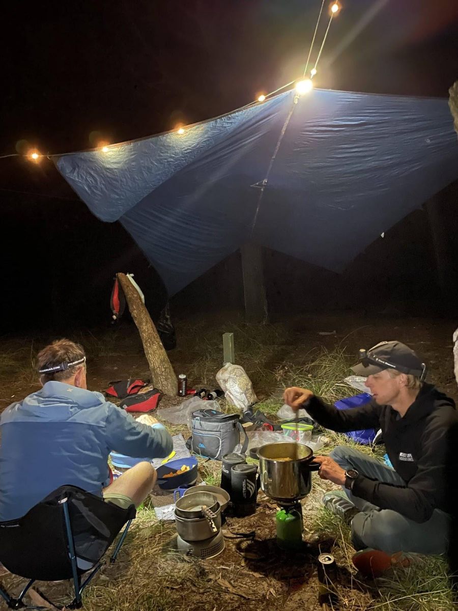 Campers at their camp kitchen at night under a tarp