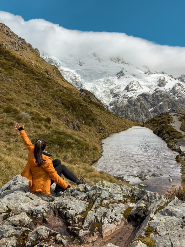 Maddie sitting on a rock wearing the Patagonia Houdini jacket with mountains in the background